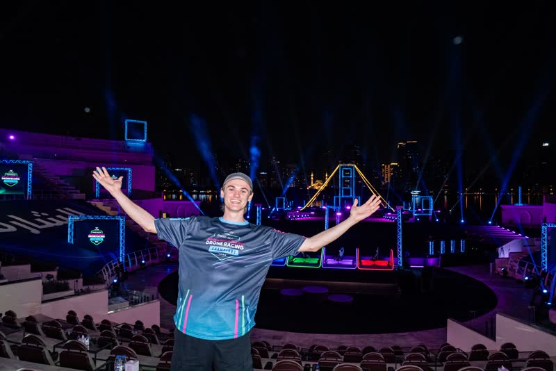 Paweł Laszczak z szeroko rozłożonymi rękami na oświetlonym stadionowym torze nocą.
